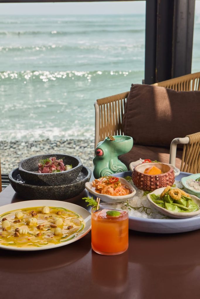 Pareja brindando con cócteles y disfrutando de comida peruana frente al mar en Cala, Lima.