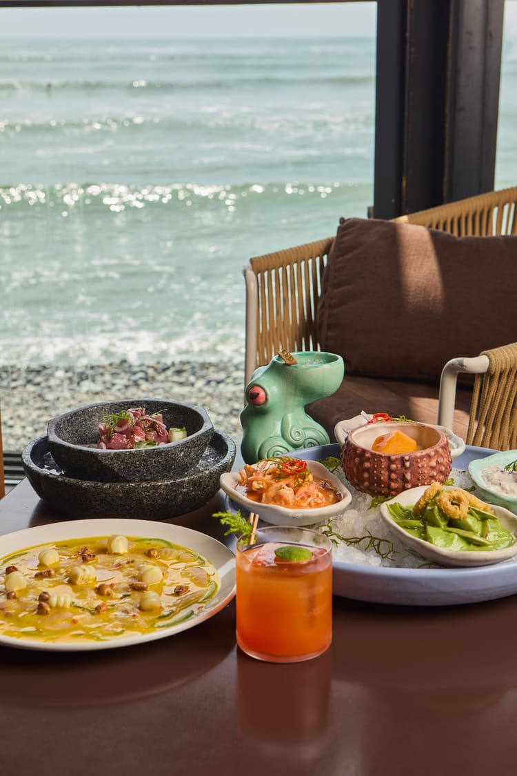 Pareja brindando con cócteles y disfrutando de comida peruana frente al mar en Cala, Lima.